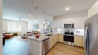 This single-floor residence showcases a thoughtfully designed open-concept layout that seamlessly connects the kitchen, dining, and living areas. The kitchen is a functional centerpiece, equipped with a full suite of stainless steel appliances, including a side-by-side refrigerator with ice and water dispenser, electric range, built-in microwave, and dishwasher. Light wood cabinetry pairs with crisp white upper cabinets and a white subway tile backsplash, while granite countertops extend across both the perimeter surfaces and a convenient kitchen island with an undermount sink. Pendant lighting above the island adds a polished finishing touch. Wood-look flooring runs throughout the main living areas, complementing the bright, neutral palette.

The living area offers comfortable proportions with natural light filtering in through windows. The bedroom features plush carpeting, a ceiling fan, a window with outdoor views, and direct access to a spacious walk-in closet outfitted with wire shelving and hanging rods. The bathroom includes a granite-topped vanity with light wood cabinetry, matching the kitchen's design language, along with wood-look flooring and a shower-tub combination. The overall ambiance is clean, contemporary, and well-coordinated throughout.