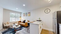 This thoughtfully designed one-bedroom, one-bathroom residence makes efficient use of its compact footprint across a single floor. The open-concept kitchen and living area serves as the heart of the space, where the kitchen features white shaker cabinetry with gold hardware, a white subway tile backsplash, stainless steel appliances including a refrigerator, dishwasher, range, and microwave, and a central island with striking granite countertops that doubles as a dining and prep area with seating for two. Light wood-tone flooring runs throughout, lending warmth and visual continuity. The living area is bright and welcoming, with a large window that invites natural light and provides views of the surrounding greenery. The bedroom is a cozy yet functional retreat, featuring a window for natural light, wood-tone flooring, and built-in shelving with in-unit laundry. The full bathroom is finished with neutral tile flooring, a granite-topped vanity with white cabinetry, and a full tub-shower combination. Clean white walls and recessed lighting throughout create a bright, modern ambiance that maximizes the sense of space.