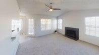 This single-story residence offers a practical and comfortable layout with a neutral color palette throughout. The spacious living room serves as the heart of the home, anchored by a sleek black fireplace with a tile surround and complemented by a modern ceiling fan with a built-in light. Multiple windows with blinds flood the space with natural light, while soft carpeting underfoot adds warmth. A glass-paneled exterior door provides additional light and access.

The kitchen is functional and well-appointed, featuring white cabinetry, subway tile backsplash, black appliances including an electric range and built-in microwave, and light wood-look flooring. A peninsula counter adds prep space and visual separation from adjacent areas. Conveniently situated just off the kitchen is a dedicated laundry area housing a full-size washer and dryer.

The bedrooms are carpeted and generously sized, each benefiting from natural light via windows. One bedroom includes a walk-in closet with built-in shelving and hanging rods, providing ample storage. The bathroom is clean and bright, with white cabinetry, a laminate countertop, a large mirror with vanity lighting, and a tub-shower combination. Textured ceilings appear throughout the home, adding a consistent finishing detail.