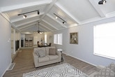 This well-appointed single-floor space combines classic architectural charm with functional design. The living area is a standout, featuring coffered ceilings with crown molding, dark hardwood-style flooring, and track lighting that highlights the room's clean lines. Two neutral-toned sofas are arranged around a geometric patterned area rug, creating an inviting and comfortable setting. Natural light filters in through windows dressed with horizontal blinds, adding brightness to the soft, light gray walls.

The dedicated office area continues the coffered ceiling motif, complemented by a ceiling fan with integrated lighting. A substantial dark wood executive desk anchors the space, while vertical blinds on a wide window provide ample light control. The hardwood-style flooring flows seamlessly throughout, tying the spaces together cohesively.

An open view from the office reveals a connecting hallway and a staircase with elegant wrought iron railing, leading to additional areas of the property. Tiled flooring in the entryway transitions smoothly into the main living spaces. A glimpse of a fitness area with equipment adds to the overall versatility of the layout. Together, the spaces offer a refined yet practical environment suited for both professional and everyday use.