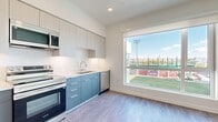 This thoughtfully designed single-floor unit offers a clean, modern aesthetic throughout its open layout. Light-toned luxury vinyl plank flooring runs continuously across the space, creating a cohesive and polished look from entry to living area.

The kitchen is a standout feature, outfitted with a two-tone cabinetry system — slate-blue lower cabinets paired with light wood-grain upper cabinets that extend toward the ceiling, maximizing vertical storage. White quartz countertops provide ample workspace, while stainless steel appliances — including a refrigerator, electric range, over-the-range microwave, and dishwasher — complete the fully functional setup. A tile backsplash adds a clean, finished touch, and a large picture window positioned at the end of the kitchen frames a striking exterior view of what appears to be a stadium or sports facility, flooding the space with natural light.

The open living area continues the airy feel, with crisp white walls, a large window offering the same dynamic outdoor views, and a ceiling vent ensuring consistent climate control.

The bathroom is finished with the same wood-look flooring and features a floating dark vanity with a white countertop, a wall-mounted towel bar, and clean, minimal fixtures — all maintaining the unit's modern design language throughout.