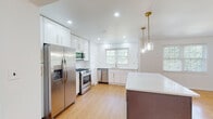 Located at 100 E Melrose Ave in Baltimore's 21212 neighborhood, this thoughtfully renovated single-floor residence blends classic architectural character with modern finishes throughout. Warm parquet hardwood floors extend across the main living areas, complementing the clean white walls and recessed lighting that give the home a bright, airy feel.

The expansive living room serves as a central gathering space, anchored by a classic fireplace with a dark tile surround and a built-in shelving unit with cabinetry on either side — a standout architectural feature that adds both charm and functionality. Natural light filters in generously through multiple windows.

The fully updated kitchen is a highlight, featuring white shaker cabinetry with gold hardware, a large central island with a contrasting dark base and quartz countertop, and a full suite of stainless steel appliances including a gas range, built-in microwave, dishwasher, and French door refrigerator. Elegant brass pendant lights hang above the island, and subway tile backsplash lines the walls. The bedrooms continue the parquet flooring aesthetic, with one room offering a built-in closet and natural views through large windows. Bathrooms are finished with marble-style tile flooring and clean white vanities with matte black hardware. An in-unit laundry area with a front-loading Whirlpool washer completes this well-appointed home.