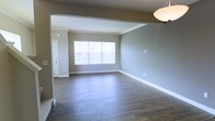 This three-floor space showcases a contemporary and understated design throughout. The main living area, as seen in the image, features wide-plank wood-look flooring that adds warmth and texture to the room while remaining low-maintenance and durable. The walls are finished in a soft, neutral grey tone that creates a calm and versatile backdrop suited to a variety of interior styles.

A large window serves as a focal point in the living area, drawing in generous amounts of natural light and offering views of the surrounding neighbourhood. The window's placement enhances the sense of openness in the room. Crisp white baseboards and trim provide clean contrast against the grey walls, contributing to a polished, well-finished appearance.

An architectural soffit detail near the ceiling adds subtle visual definition between spaces, hinting at a thoughtful open-concept layout. The smooth ceiling and recessed lighting further reinforce the modern aesthetic. With three floors of living space, this property offers ample room for a variety of functional arrangements, making it a practical and stylish option for everyday living.