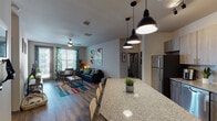 Located at 3600 E Fletcher Ave in Tampa, Florida, this single-floor residence offers a well-appointed, modern living experience. The open-concept layout seamlessly connects the kitchen and living area, creating a spacious and inviting atmosphere. The kitchen is a standout feature, equipped with stainless steel appliances — including a refrigerator, range, microwave, and dishwasher — complemented by two-tone wood cabinetry, granite countertops, a classic subway tile backsplash, and a large island with pendant lighting overhead. Wood-look flooring runs throughout the main living areas, adding warmth and continuity to the design. The living room is bright and welcoming, with access to an outdoor area through glass doors, allowing for natural light and fresh air. Ceiling fans are present throughout for comfort. The unit includes multiple bedrooms, each carpeted and thoughtfully sized, with one featuring an en-suite bathroom. A dedicated study nook with a window provides an ideal space for focused work. The bathroom is clean and functional, featuring a full tub-shower combination with tile flooring. Overall, the space presents a contemporary aesthetic with practical design choices suited for comfortable everyday living in Tampa.