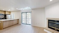 Located at 11400 College Blvd in Overland Park, Kansas, this single-floor residence showcases a clean, modern aesthetic with light wood-style flooring carried consistently throughout the space. The open living and dining area is a standout, featuring a striking skylight that floods the room with natural light alongside a full-width sliding glass door that frames lush outdoor greenery and provides easy access to the exterior. Recessed lighting complements the natural brightness, creating an airy, welcoming atmosphere. The kitchen is thoughtfully updated with warm wood cabinetry, white quartz countertops, a breakfast bar peninsula, and a full suite of stainless steel appliances including a refrigerator, range, and over-the-range microwave. A window above the counter adds additional natural light to the cooking space. The bedrooms are generously sized with crisp white walls, neutral flooring, and natural light from well-placed windows. The bathroom features tile flooring, a granite-topped vanity with white cabinetry, a large wall mirror, and a full soaking tub with tiled surround. In-unit laundry is also present, adding everyday convenience. The overall design is bright, neutral, and move-in ready.