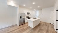 Located at 5602 Harbor Walk Way in Knoxville, Tennessee, this two-story home presents a cohesive, modern aesthetic defined by a crisp white palette and light-toned hardwood flooring that flows consistently throughout the interior. The open-concept main level centers around a well-appointed kitchen featuring white shaker-style cabinetry, stainless steel appliances including a French door refrigerator, electric range, and built-in microwave. A shiplap-accented kitchen island with an undermount sink and matte black faucet serves as a functional focal point, complemented by recessed lighting overhead. A hallway connects the kitchen area to additional rooms on the main floor, which include bright, naturally lit spaces with ceiling fans and windows overlooking the surrounding greenery. The layout, as seen in the dollhouse overview, is thoughtfully organized across both levels. Bathrooms feature white vanities with undermount sinks, matte black fixtures, and tiled shower surrounds. The upper level includes a vanity area and access to closet space. A dedicated laundry area houses a full-size washer and dryer with built-in shelving. Throughout, clean white walls, crown molding, and consistent finishes create a fresh, move-in-ready atmosphere.