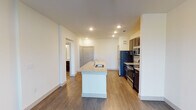 This single-floor residence is designed with a clean, contemporary aesthetic and a functional open layout. The kitchen serves as a central focal point, anchored by a large island with a granite countertop and an integrated sink, offering ample prep and seating space. Dark espresso cabinetry provides rich contrast against the light granite surfaces, while a full suite of stainless steel appliances—including a refrigerator, range, and microwave—adds a polished, modern finish. Recessed lighting illuminates the space efficiently throughout.

Wood-style plank flooring runs consistently across the main living areas, contributing to a cohesive and easy-to-maintain interior. The open floor plan connects the kitchen to the living area, creating a spacious and adaptable environment. A dedicated bedroom features dual windows that invite natural light and offer exterior views, with a ceiling fan providing added comfort.

The bathroom is well-appointed with a long dark-cabineted vanity topped with granite, a large mirror, and a walk-in shower. Crisp white walls throughout maintain a neutral, versatile backdrop. The layout, as shown in the 3D overview, demonstrates a well-organized flow between all areas of the space.