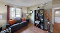 This single-floor residence offers a thoughtfully organized layout designed for comfortable everyday living. The living room serves as the heart of the home, featuring warm wood-style flooring, neutral walls, and large windows dressed with decorative curtains that invite natural light and offer outdoor views. The space accommodates multiple seating arrangements and provides a welcoming, versatile atmosphere.

The kitchen is efficiently designed with light wood cabinetry, ample counter space, a single-basin sink, a dishwasher, and a full-size refrigerator. Wood-style flooring continues through this area, adding warmth and cohesion to the space.

Two bedrooms provide restful retreats, each carpeted and finished with textured ceilings. The primary bedroom is generously sized with a closet and direct access to a bathroom, while the second bedroom features a window with outdoor views and soft, neutral tones throughout.

The bathroom is clean and functional, featuring tile flooring, a single-sink vanity with wood cabinetry, a toilet, and a shower-tub combination with a curtain enclosure. A large mirror above the vanity enhances the sense of space.

Overall, this residence presents a practical and comfortable living environment with consistent finishes, natural light, and a well-connected floor plan suited for a range of occupants.