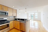 Located at 30 Haven St in Reading, MA, this one-bedroom, one-bathroom residence offers a well-designed single-floor layout that maximizes comfort and functionality. The open-concept kitchen flows seamlessly into the living area, creating a bright, connected living space. The kitchen is equipped with stainless steel appliances — including a gas range, built-in microwave, dishwasher, and refrigerator — complemented by warm maple cabinetry, dark granite countertops, a mosaic tile backsplash, and a peninsula with pendant lighting that doubles as a casual dining or prep area. Hardwood floors extend throughout the kitchen and living room, adding warmth and continuity. The living area is bathed in natural light from a large bank of windows and a sliding glass door that opens to a private balcony with outdoor views, enhanced by a track lighting fixture overhead. The bedroom features plush carpeting, ample natural light, and direct access to a walk-in closet with wire shelving for organized storage. The bathroom includes a full tub-and-shower combination with white tile surround, a decorative mosaic accent border, and tile flooring. The overall ambiance is clean, modern, and move-in ready.