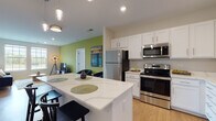 This thoughtfully designed single-floor residence offers a cohesive blend of modern finishes and comfortable living spaces. The open-concept kitchen is a standout feature, showcasing crisp white shaker cabinetry, quartz countertops with an elegant veining pattern, and a full suite of stainless steel appliances including a refrigerator, range, microwave, and dishwasher. A generous kitchen island with bar seating provides additional prep space and serves as a natural gathering point. Light wood-tone flooring runs throughout the kitchen and connects seamlessly to the living areas.

The living room is bright and welcoming, featuring large double-hung windows that frame outdoor views and fill the space with natural light. Soft carpet underfoot adds warmth and comfort to the area.

The bedrooms are well-proportioned, each offering plush carpeting, generous window placement for ample daylight, and accent walls in bold green tones that add character and energy to the rooms.

Two full bathrooms serve the residence. The primary bathroom features a long double-vanity with white cabinetry, quartz countertops, a large mirror, and wood-look flooring. The secondary bathroom is equally well-finished with white cabinetry, a single vanity, and clean, neutral tiling. Both bathrooms reflect a consistent, polished aesthetic throughout the home.
