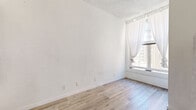 Located at 710 S Broadway in the heart of Downtown Los Angeles, this efficiently designed studio unit offers a well-utilized single-floor layout that combines the living and kitchen areas into one cohesive space. The interior features light wood laminate flooring throughout, crisp white walls, and a textured ceiling that add to the clean, minimal aesthetic.

The main living area is bright and open, anchored by a large street-facing window dressed with sheer white curtains that allow natural light to filter in and offer views of the surrounding urban architecture. A wall-mounted heating unit is conveniently positioned nearby. The soaring ceiling height enhances the sense of openness despite the compact footprint.

The kitchenette is neatly integrated into a built-in nook along one wall, featuring white cabinetry, a compact cooktop with sink, open shelving, and space for a countertop microwave — providing all essential cooking functionality in a streamlined design.

The bathroom is a separate, self-contained space finished in matching white tones with wood-look flooring. It includes a wall-mounted sink with mirror cabinet, a standard toilet, and brushed nickel hardware and towel bars for a polished finish.

This studio is ideal for those seeking a functional and low-maintenance living space in one of Los Angeles's most vibrant and well-connected urban neighborhoods.