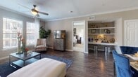 Located at 2205 Riva Row in Spring, Texas, this single-story residence offers a thoughtfully designed layout that balances comfort and functionality. The open-concept living area features rich dark hardwood flooring, crown molding, and a ceiling fan, creating a warm and inviting atmosphere. A built-in shelving unit with a dedicated bar area adds a distinctive entertaining touch to the main living space.

The kitchen is well-equipped with stainless steel appliances, including a French door refrigerator, range, and microwave. White cabinetry, light countertops, and pendant lighting over the island with bar seating contribute to a clean, modern aesthetic. Tile flooring grounds the workspace efficiently.

The bedrooms are carpeted for comfort, each featuring ceiling fans and large windows with access to a private balcony, allowing ample natural light and outdoor views. The primary suite connects to a spacious en-suite bathroom complete with a soaking tub, separate glass-enclosed shower, dual vanity, and a walk-in closet. A secondary full bathroom features a tub-shower combination with white tile surround and a single vanity, while an additional half-bath provides added convenience. The overall palette of warm taupe tones and white trim lends cohesion throughout.