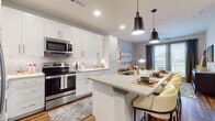 This well-designed single-floor residence offers a thoughtfully planned open-concept layout that seamlessly connects the kitchen, dining, and living areas. The kitchen is a standout feature, equipped with crisp white shaker cabinetry extending to the ceiling, a subway tile backsplash, stainless steel appliances including a range, microwave, and refrigerator, and a generous central island with a built-in sink and quartz countertop. Stylish matte black pendant lights hang above the island, which doubles as a breakfast bar with seating. Rich hardwood-style flooring runs throughout the main living areas, adding warmth and continuity to the space. The living area is bright and open, with access to an outdoor balcony and natural light filtering through large windows dressed with elegant draping curtains. The bedrooms are spacious and well-lit, each featuring large windows with blinds, ceiling fans, and the same warm hardwood-style flooring. The primary bathroom is finished with large-format tile flooring, a warm wood-toned vanity with a white countertop, and a glass-enclosed shower, with direct access to a walk-in closet offering built-in shelving and rod storage. Throughout the residence, a neutral, contemporary color palette creates a clean and cohesive aesthetic.