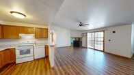 Located at 1415 Silverstone Trl in De Pere, Wisconsin, this single-floor, two-bedroom, two-bathroom home offers a comfortable and functional layout. The open-concept living and kitchen area serves as the heart of the home, featuring warm hardwood-style flooring, a ceiling fan, a gas fireplace, and a sliding glass door that fills the space with natural light and provides access to an outdoor area. The kitchen is equipped with oak cabinetry, light granite-style countertops, a double sink, and white appliances including a refrigerator, electric range, and dishwasher, with a convenient peninsula separating it from the living space. Both bedrooms are carpeted and offer a quiet, neutral atmosphere, with wood-trimmed windows allowing in natural light. The primary bedroom is a comfortable size with its own dedicated bathroom, featuring an oak vanity with a white countertop, a mirror with overhead lighting, and hardwood-style flooring. The second full bathroom mirrors this design and includes a bathtub. A hallway connects the private areas of the home, complemented by a closet for additional storage. Throughout the space, warm wood tones in the doors and trim provide a cohesive, inviting aesthetic.