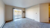 This 2-bedroom, 1-bathroom unit at 1802 40th St S in Fargo, North Dakota offers a practical and comfortable single-floor layout. The galley-style kitchen is well-appointed with warm oak cabinetry lining both walls, light wood laminate flooring, ample counter space, and includes a range, refrigerator, dishwasher, and sink — providing everything needed for everyday cooking. The kitchen flows openly into the living room, which features plush carpeting, a baseboard heating system, and a wall-mounted air conditioning unit. A full-width sliding glass door fills the living area with natural light and provides direct access to an outdoor view of the surrounding green space. Both bedrooms are carpeted and offer a quiet, neutral atmosphere, each with windows that bring in natural light. The primary bedroom includes a double-door closet for convenient storage. The full bathroom is finished with tile flooring, a wood-toned vanity with a large framed mirror, and a tub-shower combination. Throughout the unit, textured ceilings and neutral wall tones create a clean, understated backdrop. Baseboard heating is present throughout, ensuring warmth during Fargo's cold winter months.