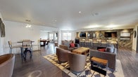 This single-floor amenity lounge is designed as a multifunctional gathering space with a cohesive industrial-modern aesthetic throughout. Rich hardwood-style flooring flows across the entire space, complementing the warm, neutral palette accented by earthy tones and bold red accessories. Recessed lighting illuminates each zone, while natural light filters in through multiple windows and glass-paneled doors.

The bar area serves as a focal point, featuring a striking herringbone reclaimed wood accent wall, a wall-mounted flat-screen TV, stainless steel refrigerator drawers, dark cabinetry, and a row of bar-height seating. Adjacent to the bar, a comfortable lounge zone offers plush gray sofas and leather swivel chairs arranged around a rustic wood coffee table atop a geometric patterned rug.

A dedicated billiards room provides ample space around a full-size pool table, accompanied by a wall-mounted TV. Nearby, a game and dining area includes a round poker-style table with upholstered chairs. Additional seating nooks throughout the space feature leather club chairs, open shelving with decorative accents, and intimate bistro tables. Framed artwork adorns the walls, contributing to the polished yet relaxed atmosphere of the lounge.
