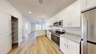 This thoughtfully designed one-bedroom, one-bathroom residence offers a bright and efficient open-concept floor plan. The kitchen is a standout feature, showcasing crisp white shaker cabinetry, speckled granite countertops, and a full suite of stainless steel appliances including a range, microwave, dishwasher, and refrigerator. A peninsula with additional cabinetry provides extra prep and storage space, while a stylish pendant light fixture adds a modern touch overhead. Light wood-tone luxury vinyl plank flooring flows seamlessly from the kitchen into the open living and dining area, which is anchored by a ceiling fan and large glass doors that invite natural light and outdoor views. A walk-in pantry with wire shelving offers generous storage off the kitchen. The bedroom is a comfortable retreat finished with plush neutral carpet, a ceiling fan, and dual windows that frame pleasant outdoor scenery. The bathroom continues the refined aesthetic with matching white cabinetry, granite countertop vanity, and wood-look flooring, and is conveniently connected to a walk-in closet with wire shelving. Throughout the unit, clean white walls, recessed lighting, and consistent finishes create a cohesive, modern ambiance.