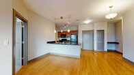 Located at 500 E Michigan Ave in Lansing, Michigan, this single-floor unit offers a thoughtfully designed open-concept layout with a seamless flow between the living and kitchen areas. Warm bamboo hardwood flooring extends throughout the main living spaces, lending a clean and contemporary feel to the interior.

The kitchen is a standout feature, equipped with rich cherry wood cabinetry, dark granite countertops, and black appliances including a refrigerator, electric range, and over-the-range microwave. A peninsula with a built-in sink and pendant lighting overhead doubles as a breakfast bar and adds to the open, airy atmosphere of the space.

The living area is generously sized and filled with natural light, with sliding glass doors opening to a private balcony that overlooks the surrounding Lansing streetscape. The bedroom areas are finished with plush carpeting and feature large double windows that frame expansive city views.

The bathroom is well-appointed, featuring a soaking tub surrounded by full tile walls in a warm earthy tone, complemented by a separate vanity area with a wood cabinet, stone-tone countertop, and large mirror. The unit also includes a dedicated entry foyer and additional interior storage, rounding out a functional and comfortable living environment.