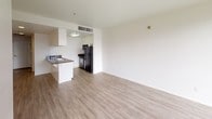 Located on the fourth floor at 770 4th Street in San Diego, unit #402 is a single-level residence featuring a bright, open-concept layout with light wood-style flooring throughout. The living area is a standout, with large floor-to-ceiling windows along two walls that flood the space with natural light and offer expansive views of the surrounding cityscape, creating an airy, urban atmosphere.

The kitchen is efficiently designed in a galley configuration and opens to the living area via a peninsula with a granite-style countertop, offering both workspace and a visual connection to the main living space. White cabinetry lines the walls, complemented by dark granite countertops, a stainless steel double sink, and black appliances including a refrigerator, electric range, and microwave. Overhead ventilation and flush-mount lighting complete the functional setup.

The bathroom maintains a clean, neutral aesthetic with light wood-style flooring that matches the rest of the unit. It features a white vanity with dark granite countertops, a large wall mirror with overhead lighting, and a full-size tub and shower combination. The overall design of the unit is clean and contemporary, with white walls and minimal detailing throughout.