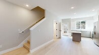 This well-designed two-story home offers 2 bedrooms and 2 bathrooms across two thoughtfully laid-out floors. The main level features an open-concept living and kitchen area bathed in natural light, with wide-plank light hardwood flooring flowing seamlessly throughout. The living room is anchored by a tile-surround fireplace and includes a wall-mounted mini-split system for efficient climate control, with windows overlooking greenery outside. The modern kitchen is a standout feature, boasting high-gloss white upper cabinetry, sleek two-tone lower cabinets, a white quartz island, subway tile backsplash, and a full suite of stainless steel appliances. A staircase with clean white trim connects the main level to the upper floor, which houses the bedrooms. The spacious primary bedroom includes direct access to an en suite bathroom with a white quartz vanity and blue-toned cabinetry. A second bedroom with large windows and a closet offers ample natural light and neighborhood views. Both bathrooms are finished with tile flooring and contemporary vanities. Neutral warm-gray walls, recessed lighting, and crisp white trim throughout lend the home a cohesive, modern aesthetic.