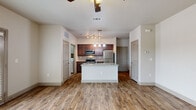 This single-story unit is designed with a functional, open-concept layout that connects the kitchen, dining, and living areas into one cohesive space. The kitchen serves as a central hub, featuring a large island with a granite countertop, an undermount double sink, and pendant lighting overhead. Rich, dark-toned cabinetry lines the kitchen walls, complemented by a tile backsplash and a full suite of stainless steel appliances, including a refrigerator, range, microwave, and dishwasher. Wood-look plank flooring extends throughout the main living areas, adding warmth and visual continuity.

The living area is spacious and bright, benefiting from natural light through a set of glass patio doors that open to an outdoor view. A ceiling fan provides additional comfort. An adjoining bedroom features plush carpeting, a window with exterior views, and its own ceiling fan. The bathroom is finished with granite-topped vanity cabinetry, wood-look tile flooring in a herringbone pattern, and a full tub-shower combination. A dedicated laundry area houses a full-size top-loading washer and dryer, adding practical convenience to the overall design.