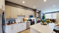 Located in Phoenix, AZ, this thoughtfully designed one-bedroom, two-bathroom residence offers an efficient and stylish single-floor layout. The open-concept kitchen and living area forms the heart of the home, featuring light wood cabinetry, white quartz countertops, a central island with bar seating, and a full suite of stainless steel appliances. Light wood-style flooring flows throughout, enhancing the cohesive, contemporary aesthetic. A standout built-in workspace neatly integrates into the kitchen area, offering a dedicated nook ideal for remote work. The living room is bright and inviting, with large windows dressed in patterned curtains that allow generous natural light, complemented by textured accent walls in a neutral gray palette. The bedroom features a ceiling fan, natural light from a window with exterior views, a patterned accent wall, and direct access to a dedicated closet. The two bathrooms are finished with white cabinetry, wood-look flooring, and bold deep-green accent walls that add a striking design element. Recessed lighting throughout the home ensures a consistently well-lit environment. This residence combines functional layout with modern design details, making it a practical and stylish living space.