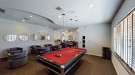 The Edge, located in Beaumont, TX, is a well-appointed community clubhouse designed to offer residents a comprehensive range of amenities within a single, thoughtfully organized floor. The welcoming entrance lobby features multicolored abstract artwork, stone-tile flooring, and comfortable seating with a reception counter nearby. Adjacent to the lobby, a spacious lounge and social area provides high-top dining tables, club chairs, and a wall-mounted TV, alongside a Coca-Cola vending machine for added convenience. A row of round decorative mirrors lines one wall, adding a contemporary design element to the lounge. The game room stands out with a full-size pool table as its centerpiece, complemented by plush barrel chairs and pendant lighting that creates an inviting atmosphere. A dedicated business center offers wrap-around built-in desks, multiple workstations, a printer, and natural light filtering through slatted blinds, making it ideal for productivity. The fitness center is equipped with treadmills, ellipticals, weight machines, ceiling fans, wall mirrors, and a mounted television. A kitchenette area features cabinetry, a microwave, and a beverage vending machine, with direct access to an outdoor pool area through a windowed door. Throughout, the space maintains a clean, modern aesthetic with neutral tones and practical finishes.