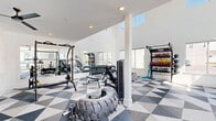 Located at 4101 William Turner Pkwy in Nashville, TN, this well-appointed fitness center offers a spacious, single-floor layout designed to support a comprehensive workout experience. The room is immediately striking thanks to its soaring double-height ceilings on one side, which flood the space with natural light through a bank of tall upper-level windows. Large standard windows along the perimeter walls frame views of the surrounding community, including an outdoor pool area visible from the cardio zone — an energizing backdrop for exercise.

The flooring throughout features a bold geometric pattern in navy, gray, and white, lending the space a modern, dynamic aesthetic that complements the crisp white walls. One accent wall showcases a textured, patterned wallcovering framed by a large mirror, adding visual depth while maximizing the sense of space.

The fitness center is fully equipped with a wide range of machines and equipment, including treadmills, ellipticals, a stair climber, stationary and rowing-style bikes, cable and multi-function strength machines, a full dumbbell rack, and adjustable benches. Ceiling fans provide additional ventilation and comfort. The layout is thoughtfully organized to keep cardio and strength training areas distinct, allowing for efficient use of the floor space while maintaining an open, uncluttered feel.