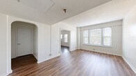 Located at 1 E 36th St in Indianapolis, IN, this two-bedroom, one-bathroom unit offers a practical and comfortable single-floor layout. Warm-toned hardwood-style flooring runs throughout, providing a cohesive look across all rooms.

The living room is a bright, open space featuring a charming arched doorway, crisp white walls, and multiple windows that invite generous natural light. A doorway leads directly into a second room, enhancing the sense of flow and connectivity throughout the unit.

The kitchen is well-appointed with rich, warm wood cabinetry extending to the upper walls for ample storage, light countertops, and a full suite of white appliances including a refrigerator, dishwasher, and range. A pendant light fixture overhead and a side window add character and brightness to the space.

Both bedrooms are comfortably sized with neutral walls and hardwood-style flooring. The primary bedroom features a large triple-pane window with views of the surrounding neighborhood, filling the room with natural light. The second bedroom also benefits from window access and connects conveniently to the hallway.

The bathroom is clean and functional, featuring white tile surround on the tub-shower combination, a vanity with wood cabinetry, a mirror, and a window for natural ventilation. Two hallways connect the rooms efficiently, completing this well-organized and inviting layout.