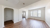 Located at 1 E 36th St in Indianapolis, IN, this two-bedroom, one-bathroom unit offers a practical and comfortable single-floor layout. Warm-toned hardwood-style flooring runs throughout, providing a cohesive look across all rooms.

The living room is a bright, open space featuring a charming arched doorway, crisp white walls, and multiple windows that invite generous natural light. A doorway leads directly into a second room, enhancing the sense of flow and connectivity throughout the unit.

The kitchen is well-appointed with rich, warm wood cabinetry extending to the upper walls for ample storage, light countertops, and a full suite of white appliances including a refrigerator, dishwasher, and range. A pendant light fixture overhead and a side window add character and brightness to the space.

Both bedrooms are comfortably sized with neutral walls and hardwood-style flooring. The primary bedroom features a large triple-pane window with views of the surrounding neighborhood, filling the room with natural light. The second bedroom also benefits from window access and connects conveniently to the hallway.

The bathroom is clean and functional, featuring white tile surround on the tub-shower combination, a vanity with wood cabinetry, a mirror, and a window for natural ventilation. Two hallways connect the rooms efficiently, completing this well-organized and inviting layout.