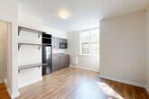 Located at 3635 Phinney Ave N in Seattle's vibrant Phinney Ridge neighborhood, this studio unit offers a thoughtfully designed single-floor layout that efficiently combines living, dining, and kitchen functions into one open space. Warm-toned luxury vinyl plank flooring runs throughout, creating a cohesive and easy-to-maintain foundation. A large window floods the living area with natural light and frames views of surrounding greenery, lending an airy feel to the compact footprint. The kitchenette is outfitted with dark-toned cabinetry, a stainless steel refrigerator, an under-cabinet sink, a built-in microwave, and a wall-mounted baseboard heater nearby. Open wall shelving adjacent to the kitchen provides additional storage and display space. The main living area features clean white walls and a neutral palette, offering a versatile canvas for various furniture arrangements. An electrical panel is conveniently integrated near the entry door. The bathroom features large-format white subway tile in the shower/tub surround, complete with a recessed niche for toiletries and a glass door enclosure, presenting a clean and modern aesthetic. Overall, the unit delivers a minimalist, contemporary design well-suited for efficient urban living.