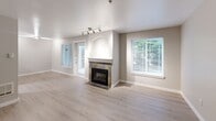 Located in Federal Way, WA, this single-floor, 3-bedroom, 2-bathroom home offers a well-designed layout that balances comfort and functionality. The open-concept living, dining, and kitchen area serves as the heart of the home, featuring light wood-style flooring, a tile-surround fireplace with a classic white mantel, and large windows fitted with blinds that invite natural light. Track lighting above adds a modern touch to the living space, which also provides direct access to a private patio.

The kitchen is equipped with light wood cabinetry, granite-look countertops, white appliances including a range, microwave, and refrigerator, and an arched pass-through window that connects to the dining area — a charming architectural detail that enhances the open feel.

The three bedrooms feature plush wall-to-wall carpeting, natural light from windows, and baseboard heating. The generously sized primary bedroom connects to a well-appointed bathroom. Two full bathrooms serve the home: one with a walk-in glass shower and the other with a tub-shower combination, both finished with light wood-look flooring and granite-look vanity countertops.

Additional highlights include six closets, a pantry, a dedicated laundry room, a utility room, and a central hallway that ties the layout together efficiently.