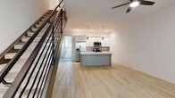 This well-appointed two-story residence combines modern design with functional living across two thoughtfully laid-out floors. The main level centers around an open-concept living and kitchen area, where light wood-style flooring flows throughout. The kitchen is a standout feature, showcasing a large center island with a light gray base, white quartz countertops, white shaker-style cabinetry, a mosaic tile backsplash, and a full suite of stainless steel appliances including a side-by-side refrigerator, microwave, and range. Pendant lighting hangs above the island, complemented by recessed ceiling lights and a ceiling fan in the living area. A sliding glass door with vertical blinds allows natural light to pour in and provides outdoor access. A staircase with a sleek metal railing connects the two floors. The upper level features multiple bedrooms finished with plush neutral carpeting and blinds-covered windows that invite abundant natural light. The bathrooms are finished with wood-look tile flooring, white shaker vanities, quartz countertops, brushed gold fixtures, and tub-shower combinations with white tile surrounds. Throughout, the space maintains a clean, neutral palette that creates a bright and welcoming atmosphere.
