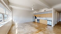 This one-bedroom, one-bathroom unit in downtown Baton Rouge, LA offers a modern, urban aesthetic defined by clean lines and an open-concept design. The main living area is expansive and sun-drenched, highlighted by polished concrete floors, elevated ceilings with exposed beams, and a ceiling fan that enhances the airy feel. A wide bank of floor-to-ceiling windows frames impressive cityscape views, flooding the space with natural light throughout the day.

The kitchen runs along one wall in a galley-style configuration, equipped with light wood cabinetry extending to the ceiling, stainless steel appliances including a refrigerator, electric range with oven, and dishwasher, along with light-toned countertops and a stainless sink with a sleek backsplash.

A well-lit hallway connects the main living area to the private quarters. The bedroom features dark carpet flooring, a ceiling fan, a spacious sliding-door closet, and clerestory windows that bring in additional light. The full bathroom is finished with dark slate tile flooring, a wood-framed open vanity with a white basin sink, and a separate tub and shower combination with white tile surround. The overall design reflects a contemporary, minimalist sensibility throughout.