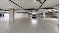 Located at 2673 Trinity St in Abbotsford, BC, this expansive underground parkade offers a substantial, single-level footprint designed to serve a multi-unit residential building. The facility is thoughtfully organized, with clearly marked parking stalls — including designated accessible spaces and small-car stalls — distributed across the open concrete floor, which features a smooth, light-toned epoxy-style coating throughout.

Structural concrete columns punctuate the space at regular intervals, supporting the overhead ceiling fitted with a spray-applied fireproofing texture. An extensive network of pipes, conduits, and mechanical systems runs across the ceiling, all neatly organized and complemented by fluorescent strip lighting that ensures consistent illumination throughout the facility.

Vehicle access is provided via a secured gate entrance equipped with safety bollards finished in high-visibility yellow. A dedicated secured area separated by chain-link fencing serves as bicycle storage, accommodating a variety of bikes and offering additional wall-mounted hooks for further convenience. Wheel stops finished in black and yellow are positioned throughout the stalls to guide and protect parked vehicles.

Interior access doors connect the parkade to the building's interior, and clearly posted exit signage ensures safe navigation throughout. The overall design prioritizes functionality, safety, and efficient use of space for both vehicle and bicycle parking.