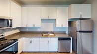This single-floor residence offers a clean, modern aesthetic with a thoughtfully designed layout. The open-concept living area flows seamlessly into the kitchen, where white flat-panel cabinetry with brushed nickel hardware provides ample storage. The kitchen is equipped with stainless steel appliances, including a range, over-the-range microwave, and dishwasher, complemented by a double-basin sink and neutral-toned countertops. Light wood-style flooring grounds the living and kitchen spaces, adding warmth to the crisp, neutral palette.

The bedrooms feature plush carpeting, ceiling fans, and multiple windows that allow natural light to fill each room. At least one bedroom includes a dedicated closet with built-in hanging storage. The darker wood-toned flooring in one room adds a subtle contrast to the overall design.

Two full bathrooms serve the unit, each featuring white vanity cabinetry, neutral countertops, and tub-shower combinations. One bathroom benefits from a large window that introduces natural light, while the other is appointed with a multi-bulb vanity light fixture above the mirror. Tile flooring completes each bathroom's functional and polished look. The overall design prioritizes clean lines, neutral tones, and practical finishes throughout.