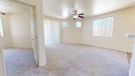 This single-story, 3-bedroom, 2-bathroom home offers a practical and comfortable layout across a well-utilized floor plan. The combined kitchen and living room serves as the heart of the home, featuring light wood-toned cabinetry, white appliances including a refrigerator, range, microwave, and dishwasher, and wood-look flooring that extends through the kitchen area. A breakfast bar provides a convenient transition into the adjacent living space, which is finished with plush carpeting, a ceiling fan with light fixture, and multiple windows dressed with vertical blinds that allow for ample natural light. A sliding glass door opens to an outdoor area, further brightening the living space. Each of the three bedrooms is carpeted and features a ceiling fan, as well as a sliding-door closet with built-in hanging rods. The primary bedroom includes direct access to one of the two bathrooms, which offers a single-sink vanity with light wood cabinetry, a large mirror, and tile-surround shower. A dedicated laundry room houses a full-size washer and dryer with overhead shelving. The hallway connects all rooms efficiently, and an additional closet provides supplemental storage. Neutral warm-beige tones throughout create a cohesive and inviting atmosphere.