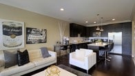 Located at 20 E. Hubbard Ave in Columbus, Ohio, this single-floor residence offers a seamlessly connected open-concept layout designed for modern living. The living area is anchored by crisp white upholstered seating, dark hardwood flooring, and warm neutral walls accented with crown molding, creating an inviting and polished atmosphere. Recessed lighting throughout ensures the space is bright and well-illuminated at all times. The living area flows naturally into a sophisticated kitchen, which features dark espresso cabinetry reaching toward the ceiling, stainless steel appliances, and a light-toned countertop that provides striking contrast. A kitchen island with bar seating serves as both a functional workspace and a casual dining spot, while pendant lights hanging above add a refined, contemporary touch. A compact dining area nestled between the kitchen and living space offers an intimate setting for meals. The cohesive design language — pairing dark cabinetry and flooring with bright furnishings and neutral walls — lends the entire floor a bold yet balanced aesthetic. This urban residence combines practical functionality with upscale design, making it well-suited for those seeking a stylish home in a prime Columbus location.