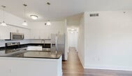 Located in Princeton, FL, this well-appointed residence offers three bedrooms, two bathrooms, and a thoughtfully designed single-floor layout. The open-concept kitchen serves as the heart of the home, showcasing white shaker cabinetry, dark granite countertops, a subway tile backsplash, and a full suite of stainless steel appliances including a range, microwave, dishwasher, and French door refrigerator. Pendant lighting illuminates the kitchen island, which provides additional prep and dining space. The combined dining and living area flows naturally from the kitchen, featuring warm hardwood-style flooring and sliding glass doors that open to a private balcony with outdoor views. The bedrooms are well-sized, each offering hardwood-style floors, natural light from windows with blinds, and louvered closet doors leading to dedicated closet spaces. Four closets total provide ample storage throughout the unit. Both bathrooms are finished with dark granite vanity tops, dark cabinetry with modern hardware, large-format tile flooring, and tiled tub-shower combinations. Additional conveniences include a dedicated laundry area and a utility room, rounding out this functional and modern residence.