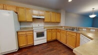 Located at Lake Pointe Village Circle in Orlando, Florida, this two-floor residence offers a thoughtfully arranged layout with a blend of practical finishes and comfortable living spaces. The main level centers around an open-concept kitchen and living area, where rich, dark hardwood-style flooring flows throughout. The kitchen is well-equipped with warm honey-toned wood cabinetry extending to the upper walls, light stone-toned countertops, a full suite of white appliances including a refrigerator with ice maker, electric range with hood, and dishwasher, all complemented by a double sink and a curved peninsula that defines the dining space. A pendant light fixture anchors the dining area, while natural light filters in through windows overlooking the surroundings. The bathrooms feature matching wood vanities with light countertops, tile flooring, and tub-shower combinations. The bedrooms are carpeted for comfort, with the primary bedroom offering direct access to an en-suite bathroom and an additional walk-in closet area. Neutral wall tones and clean white trim carry throughout the home, creating a cohesive and move-in-ready atmosphere across both floors.