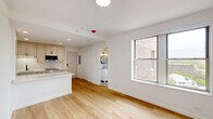 Located at 2140 North Lincoln Park West in Chicago's sought-after Lincoln Park neighborhood, this thoughtfully designed studio offers a clean, modern aesthetic across its single-floor layout. Light-toned hardwood flooring runs seamlessly throughout, lending warmth and continuity to the open-concept space.

The kitchen is a standout feature, showcasing a galley-style configuration with shaker-style cabinetry in a soft greige finish, white quartz countertops, a matte black faucet with undermount stainless steel sink, and stainless steel appliances including a refrigerator, range, and dishwasher. A central kitchen island provides additional prep and storage space, flowing naturally into the living area. Recessed lighting and a bright, neutral palette keep the space feeling open and airy.

The living area benefits from multiple windows offering views of the surrounding urban neighborhood, allowing ample natural light to fill the room. White walls and a clean architectural design maximize the sense of space.

The bathroom is particularly well-appointed, featuring hexagonal patterned tile flooring, textured white wall tiles, a glass-enclosed walk-in shower with matte black fixtures, a white vanity, and a round mirror — combining contemporary style with functional design. This unit is ideally situated near Lincoln Park's amenities, dining, and transit options.