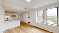Located at 2140 North Lincoln Park West in Chicago's sought-after Lincoln Park neighborhood, this thoughtfully designed studio offers a clean, modern aesthetic across its single-floor layout. Light-toned hardwood flooring runs seamlessly throughout, lending warmth and continuity to the open-concept space.

The kitchen is a standout feature, showcasing a galley-style configuration with shaker-style cabinetry in a soft greige finish, white quartz countertops, a matte black faucet with undermount stainless steel sink, and stainless steel appliances including a refrigerator, range, and dishwasher. A central kitchen island provides additional prep and storage space, flowing naturally into the living area. Recessed lighting and a bright, neutral palette keep the space feeling open and airy.

The living area benefits from multiple windows offering views of the surrounding urban neighborhood, allowing ample natural light to fill the room. White walls and a clean architectural design maximize the sense of space.

The bathroom is particularly well-appointed, featuring hexagonal patterned tile flooring, textured white wall tiles, a glass-enclosed walk-in shower with matte black fixtures, a white vanity, and a round mirror — combining contemporary style with functional design. This unit is ideally situated near Lincoln Park's amenities, dining, and transit options.