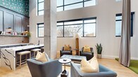 Located at 2025 Cleveland Ave in Charlotte's vibrant South End neighborhood, this single-floor amenity space offers a thoughtfully designed and versatile environment. The space is defined by its dramatic double-height ceilings and an abundance of natural light pouring in through large, black-framed windows that frame views of the surrounding Charlotte cityscape.

The open lounge area features light hardwood flooring, exposed concrete columns, and a curated mix of contemporary seating — including plush gray and blue upholstered chairs accented with gold throw pillows — creating an inviting and stylish gathering space. A dark bookcase provides both decorative and functional storage, complementing the modern industrial aesthetic.

A dedicated golf simulator bay offers a premium recreational experience, complete with artificial turf flooring, a full projection screen, and an adjacent lounge outfitted with patterned wallcovering and comfortable seating for spectators.

The kitchen is well-appointed with rich, wood-toned cabinetry, striking white marble-look quartz countertops, a hexagonal penny tile backsplash, open shelving with warm accent lighting, and stainless steel appliances — designed to support both casual and catered use. The overall ambiance balances industrial architecture with refined, modern finishes throughout.