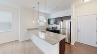 Located in Georgetown, Delaware, this single-floor, one-bedroom, one-bathroom residence offers a thoughtfully designed layout with modern finishes throughout. The open-concept kitchen is a standout feature, boasting granite countertops, dark cabinetry, stainless steel appliances — including a refrigerator, electric range, and microwave — and a peninsula island illuminated by stylish pendant lighting. The kitchen flows seamlessly into the living area, which features plush carpeting, a ceiling fan, and multiple windows that invite natural light. Hardwood-style flooring in the kitchen and bathroom areas adds a clean contrast to the soft carpet elsewhere. The bathroom includes a full tub-shower combination, a granite-topped vanity with dark cabinetry, and wood-style flooring. The generously sized primary bedroom features a ceiling fan, a wall-mounted climate control unit, and dual bi-fold closets providing ample storage. A hallway connects the spaces efficiently, contributing to the home's functional flow. Neutral tones and clean finishes throughout create a bright, welcoming ambiance, making this residence a comfortable and practical home in Georgetown, DE.