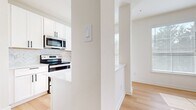 This single-floor space is designed with a clean, contemporary aesthetic, characterized by crisp white walls, light hardwood flooring, and an abundance of natural light. The open layout connects key living areas seamlessly, creating a bright and airy atmosphere throughout.

The living room serves as a central gathering space, anchored by a white-mantled fireplace and large windows fitted with horizontal blinds that filter generous amounts of natural light. The room's generous proportions and high ceilings enhance the sense of openness.

The kitchen is well-appointed with white shaker-style cabinetry featuring matte black hardware, a herringbone-patterned tile backsplash, and a full suite of stainless steel appliances including a refrigerator, electric range, and over-the-range microwave. A kitchen island with a white countertop provides additional workspace and a natural division between the kitchen and adjacent areas.

The bedrooms continue the light-filled theme, each featuring hardwood flooring, white walls, and sizable windows. One bedroom includes a ceiling fan and another connects directly to a walk-in closet with wire shelving. An additional dedicated walk-in closet provides further storage capacity. The overall ambiance is clean, modern, and move-in ready.
