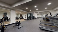 Located at 1825 Galindo St in Concord, California, this single-floor fitness center is thoughtfully designed to accommodate a comprehensive range of workout activities. The space is organized into several distinct functional zones, providing a structured environment for varied training needs.

The main workout area features durable rubber flooring throughout and is illuminated by recessed ceiling lights, creating a bright, consistent atmosphere. A robust selection of strength training equipment is distributed across the floor, including cable machines, weight benches, and a rack system, complemented by a dedicated dumbbell station positioned along a mirrored wall that enhances the sense of depth and space.

The cardio zone houses multiple treadmills, elliptical trainers, stationary bikes, and rowing machines, arranged in an orderly layout that allows for comfortable circulation between equipment. A separate functional training area features light wood flooring, floor-to-ceiling mirrors, stability balls, and aerobic step platforms, providing an open space well-suited for stretching, group exercise, or bodyweight training.

Throughout the facility, clean white walls and a neutral color palette contribute to a modern, professional ambiance. The thoughtful zoning of equipment and the generous overall footprint make this fitness center a versatile and well-appointed space for a wide range of users.