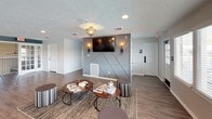 The Lake Castleton clubhouse is a thoughtfully designed single-floor community gathering space that blends modern aesthetics with practical amenities. The interior is finished with warm hardwood-style flooring that flows consistently throughout, tying together each distinct area of the space.

The kitchen is a standout feature, outfitted with crisp white shaker cabinetry accented by matte black hardware. Dark granite-style countertops provide a striking contrast, while the mosaic tile backsplash adds visual texture. Black appliances, including a range, microwave, and dishwasher, complement the contemporary color palette. A peninsula with bar seating and pendant lighting overhead makes the space both functional and social. A wall-mounted cue rack hints at recreational use nearby.

Adjacent to the kitchen, a welcoming lounge area features a geometric wainscoted accent wall in cool gray tones, a wall-mounted flat-screen television, and stylish sconce lighting. Comfortable seating arrangements with round coffee tables and area rugs create an inviting atmosphere, while a row of windows along one wall brings in abundant natural light.

The dining area is finished in calming blue-gray tones with white beadboard wainscoting, multiple wall-mounted screens, and patterned wallcovering accents. French doors provide easy access, enhancing the room's open and airy feel. Elegant flush-mount light fixtures with gold detailing add a refined touch throughout.