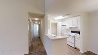 Located at 17830 Baldwin Farms Pl in Robertsdale, Alabama, this single-story home offers a straightforward and functional layout designed for everyday living. The kitchen is a central feature of the space, showcasing white cabinetry that extends to the upper walls, providing ample storage. A peninsula with a built-in sink serves as both a prep area and a natural divider between the kitchen and adjoining living spaces, enhancing the open feel of the home. White appliances, including a range and refrigerator, complement the clean, bright aesthetic of the kitchen area. The flooring transitions from wood-look planks in the kitchen and entry areas to carpet further down the hallway, adding warmth to the private areas of the home. A long hallway extends from the main living area, lined with doors leading to individual rooms, each benefiting from natural light filtering through windows. The textured ceilings and neutral wall tones throughout create a consistent, move-in-ready atmosphere. Overall, the home presents a practical and well-lit interior suited for comfortable, single-level living.