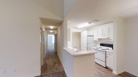 Located at 17830 Baldwin Farms Pl in Robertsdale, Alabama, this single-story home offers a straightforward and functional layout designed for everyday living. The kitchen is a central feature of the space, showcasing white cabinetry that extends to the upper walls, providing ample storage. A peninsula with a built-in sink serves as both a prep area and a natural divider between the kitchen and adjoining living spaces, enhancing the open feel of the home. White appliances, including a range and refrigerator, complement the clean, bright aesthetic of the kitchen area. The flooring transitions from wood-look planks in the kitchen and entry areas to carpet further down the hallway, adding warmth to the private areas of the home. A long hallway extends from the main living area, lined with doors leading to individual rooms, each benefiting from natural light filtering through windows. The textured ceilings and neutral wall tones throughout create a consistent, move-in-ready atmosphere. Overall, the home presents a practical and well-lit interior suited for comfortable, single-level living.