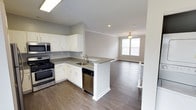This 3-floor home is designed with a clean, modern aesthetic that emphasizes open living and functional flow. The main living level showcases an open-concept layout where the kitchen connects seamlessly to the living area, creating a spacious and cohesive environment well-suited for everyday living and entertaining.

The kitchen is appointed with white shaker-style cabinetry that extends to the upper walls, complemented by grey countertops that provide a neutral, contemporary contrast. A peninsula with a built-in sink extends from the main counter, offering additional workspace and a natural dividing point between the kitchen and living area. Stainless steel appliances, including a gas range, microwave, and dishwasher, complete the kitchen's functional layout. A skylight above the kitchen brings in additional natural light, brightening the space considerably.

The adjoining living area continues the hardwood-style flooring found throughout and features crown molding, recessed lighting, and a ceiling fan. A window at the far end of the living space allows natural light to filter in, contributing to the home's airy, welcoming ambiance. Neutral grey-toned walls throughout provide a versatile backdrop adaptable to a variety of interior styles.